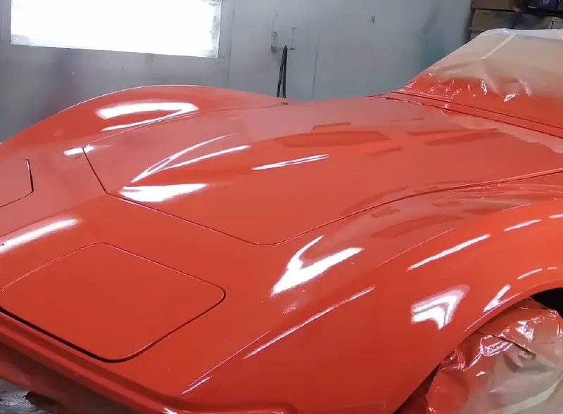 A classic car freshly painted bright orange, glossy and masked off, in the shop's paint booth